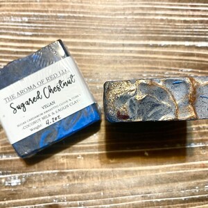 May include: A blue and black bar of soap with gold flecks. The soap is labelled "The Aroma of Red Lia Sugared Chestnut Vegan Sugar Cardamom Amaretto Clove & Tone - Coconut Milk & Kaolin Clay Weight: 4.2 oz"