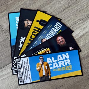 May include: A fan of rectangular event tickets featuring various comedians. The top ticket shows Alan Carr with the text 'ALAN CARR HAVE I SAID TOO MUCH?' in white and yellow, including a barcode, date 03.05.26, and venue details on a blue background.