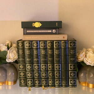 May include: A stack of books on a shelf, including "Oprah Winfrey What I Know For Sure" and "Collected Poems W.B. Yeats".  Two grey ceramic vases with white roses are on either side of the books.
