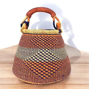 May include: A woven basket with a leather handle. The basket is orange, yellow, and blue with a geometric pattern.