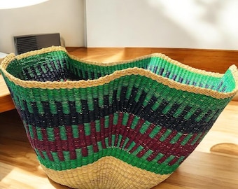 May include: A large, woven basket with a wavy rim. The basket features a geometric pattern in green, black, and burgundy, with a natural tan base and rim. The basket is made of natural fibers and is suitable for storage or decoration.