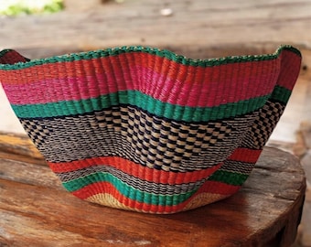 May include: A large, woven basket with a wavy rim. The basket is made of natural fibers and has a colorful striped pattern in shades of pink, red, green, and black.