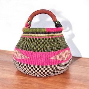 May include: A large, woven basket with a pink, green, and black geometric pattern. The basket has a brown leather handle.