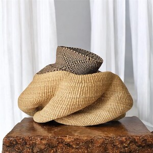 May include: A woven straw hat with a black and white geometric pattern. The hat is folded and twisted into a unique shape.