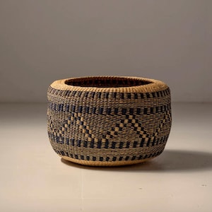 May include: A woven basket with a geometric pattern in shades of brown and blue. The basket is round and has a wide opening.