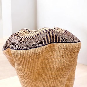 May include: A large, woven basket with a brown and black geometric pattern. The basket is made of natural materials and has a rounded, organic shape.