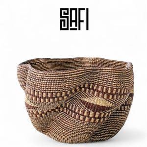 May include: A handwoven basket with an unusual, curved form. The basket is made from natural fibres in brown and beige tones, featuring a repeating design. The word "SAFI" is printed in black above the basket.