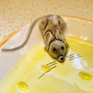 May include: A ceramic serving dish featuring a three-dimensional gray mouse sculpture attached to the rim. The interior of the dish is painted a bright yellow with painted black whiskers extending from the mouse's snout onto the yellow surface.