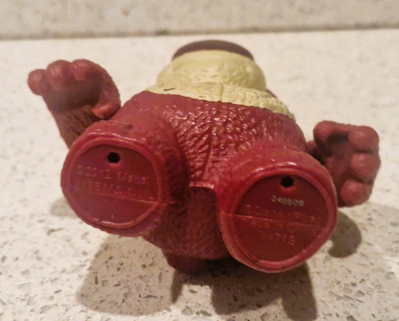 Peut inclure: Figurine jouet rouge et beige avec une surface textur&eacute;e. La figurine a deux pieds rouges avec des indentations circulaires et du texte. La figurine a deux bras et une t&ecirc;te avec un dessus beige.