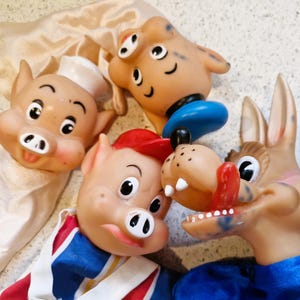 May include: A collection of vintage rubber hand puppets featuring cartoon pig and donkey characters. The puppets have painted details, including rosy cheeks, hats, and clothing. The puppets are in various colors, including tan, red, blue, and white.