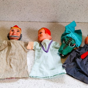 May include: Five hand puppets, including a green alligator, a man with a striped robe and a red hat, a woman with a blue and white dress, a green alligator with a blue hat, and a man with a blue hat and a red tie.