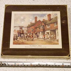 May include: A framed print of "The George Inn, Crawley" featuring a horse-drawn carriage and people in front of a brick building. The print is set in a brown frame and is in a box. The ruler shows the frame is about 9 inches long.