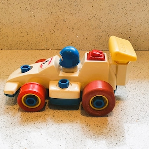 Könnte beinhalten: Ein weißes Spielzeug-Rennwagen mit roten und blauen Akzenten. Das Auto hat einen gelben Spoiler und einen blauen Helm oben drauf. Das Auto hat die Nummer 8 an der Seite.