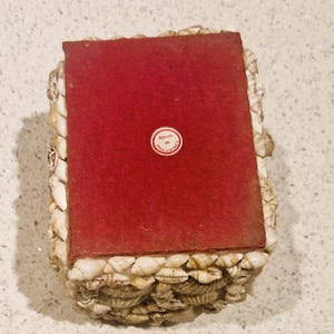 May include: A rectangular box decorated with small, white seashells. The top is a solid, deep red colour. A small, circular sticker on the top reads "MADE IN PHILIPPINES".