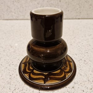 May include: A brown ceramic candle holder with a white interior and a decorative brown and white pattern on the base.