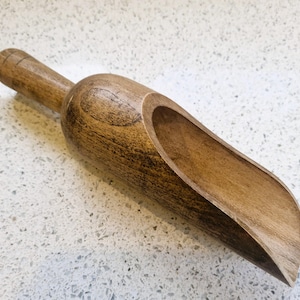 Peut inclure: Une louche en bois avec un long manche et une cuvette incurvée et profonde. La louche est en bois brun clair avec des motifs de grain brun plus foncé. Le manche est cylindrique avec une extrémité arrondie. La louche est conçue pour prélever des produits secs.