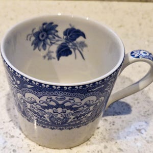 以下が含まれることがあります： 内側に青い花柄、外側に詳細な青い模様が施された白いティーカップ。 ハンドルにも青い花柄があります。 カップはセラミック製です。