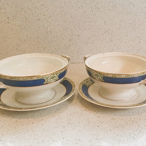 May include: Two white porcelain soup tureens with blue and gold trim and lids. Each tureen is on a matching saucer.