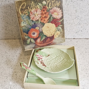 Puede incluir: Un plato verde en forma de hoja con un diseño floral y una cuchara a juego en una caja con las palabras "Carlton Ware" impresas en la tapa.