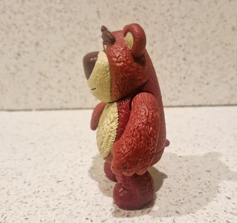 Peut inclure: Figurine d'ours rouge et beige avec une texture. L'ours a un nez brun fonc&eacute;, un ventre beige clair et une petite corne brun fonc&eacute;. La figurine est pos&eacute;e sur une surface blanche.