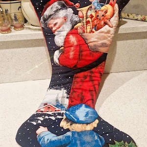 May include: Vintage Christmas stocking with a quilted design. Features Santa Claus, a child, and a teddy bear. The stocking is primarily navy blue with red and white accents, and the words "Christmas Greetings".
