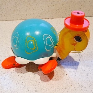 May include: A blue and yellow toy turtle with a red hat. The turtle has a smiling face and is made of plastic.