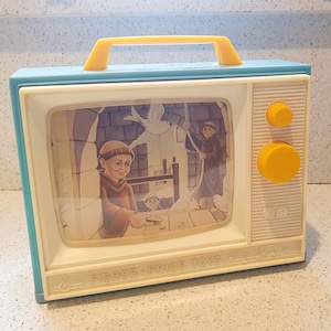 Op de afbeelding: Een vintage Fisher-Price Toys speelgoedtelevisie van blauw en wit plastic met een gele handgreep. Het scherm toont een cartoonbeeld van drie mensen in middeleeuwse kleding. Het speelgoed heeft twee ronde gele knoppen aan de zijkant.