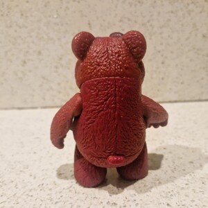 Peut inclure: Figurine d'ours en peluche de couleur marron, vue de dos. L'ours a une surface textur&eacute;e, de petites oreilles et des bras et des jambes trapus. La figurine est pos&eacute;e sur une surface de couleur claire.