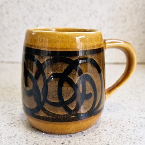 May include: A brown ceramic mug with a black and brown swirling design. The mug has a rounded body and a handle.