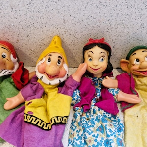 Puede incluir: Cuatro marionetas de mano vintage con personajes de Blancanieves. Las marionetas incluyen un enano con sombrero rojo y atuendo verde, un enano con sombrero amarillo y atuendo morado, Blancanieves y otro enano con sombrero verde.