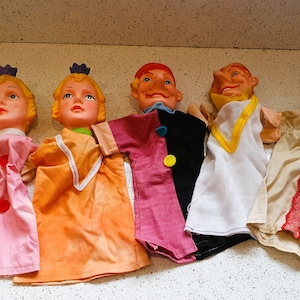 Puede incluir: Conjunto de cinco marionetas de mano vintage. Dos marionetas femeninas con cabello rubio y vestidos rosa y naranja. Tres marionetas masculinas con ropa roja, blanca y beige.