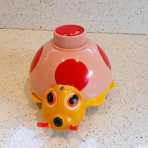 May include: A pink ladybug toy with red spots and a yellow head with black eyes. The ladybug has a small, round, pink button on top.