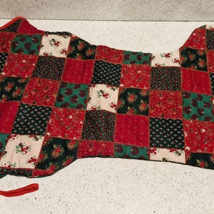 May include: A quilted saddle pad with a patchwork design. The pad features squares of red, green, black, and cream fabric with floral patterns. The edges are trimmed with red fabric and a red tie.
