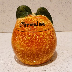 May include: A ceramic marmalade jar shaped like an orange with a green leaf design on the lid. The jar is decorated with brown speckles and the word "Marmalade" is written on the lid.