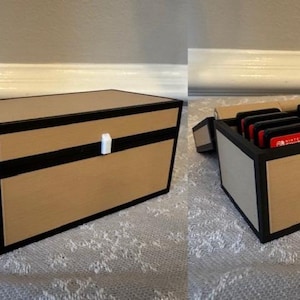 May include: A rectangular wooden box with a light brown finish and black trim. The box is closed with a white latch. The box is open in the second image, revealing several red and black game cartridges.