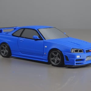 Könnte beinhalten: Ein blaues Sportwagen-Modell mit Heckspoiler, grauen Fünfspeichenrädern und einem Frontgrill mit sichtbarem Ladeluftkühler. Das Fahrzeug hat eine Coupé-Karosserieform mit schwarzen Fensterrahmen und einem detaillierten Frontstoßfänger.