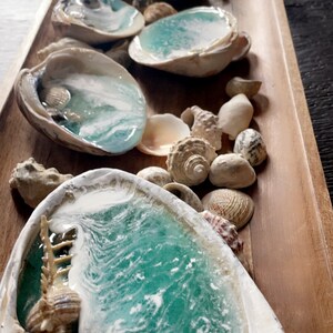 May include: A wooden tray with seashells and four seashell dishes filled with turquoise blue resin that resembles ocean waves. The resin is clear and has white swirls that look like foam.
