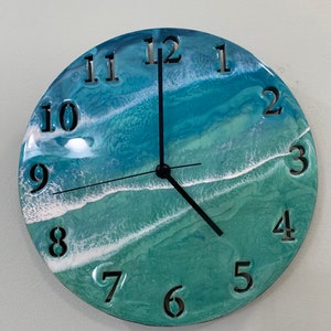 May include: A round clock with a blue, green, and white ocean wave design. The clock face has black hands and black numbers 1 through 12.