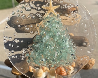 May include: A clear round ornament with a green glass Christmas tree inside. The tree is decorated with a gold starfish and seashells.