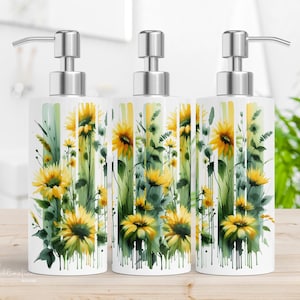 May include: Three white ceramic soap dispensers with stainless steel pumps. Each dispenser features a watercolor design of yellow sunflowers and green foliage. The dispensers are arranged on a wooden surface.