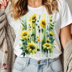 May include: White t-shirt with a watercolor design of sunflowers and greenery. The design is in shades of yellow, green, and brown.