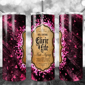 Könnte beinhalten: Drei Edelstahlbecher mit Strohhalmen. Die Becher haben ein dunkelrosa-schwarzes Design mit rosa Glitzer und Vogelsilhouetten. Der mittlere Becher trägt die Aufschrift "100% Organic Elixir of Life Anti-Aging."