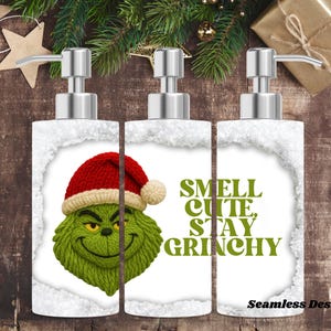 May include: Three white soap dispensers with silver pumps. Each dispenser features a Grinch design wearing a Santa hat. The text "SMELL CUTE, STAY GRINCHY" is printed on the center dispenser. The words "Seamless Design" are printed at the bottom.