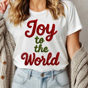 May include: White t-shirt with the text "Joy to the World" in red and green embroidered lettering. The shirt is a classic crew neck style and is made of a soft material. The design is festive and suitable for the holiday season.