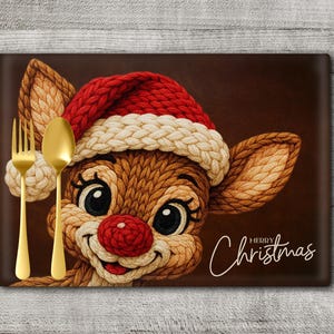 Op de afbeelding: Een rechthoekige placemat met een cartoon rendier met een kerstmuts, rode neus en lachend gezicht. De placemat heeft een bruine achtergrond met de woorden "Merry Christmas" in witte letters. Een gouden vork en lepel staan links.