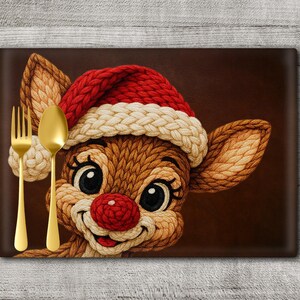 Op de afbeelding: Een rechthoekige placemat met een cartoon rendier met een rood-witte kerstmuts. Het rendier heeft een rode neus en lacht. Een gouden vork en lepel staan links. De achtergrond is bruin.