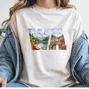 May include: Off-white t-shirt featuring the letters "WA" filled with watercolor images of a mountain range, lake, apples, and pink flowers. The shirt is made of a soft material and has a crew neck.