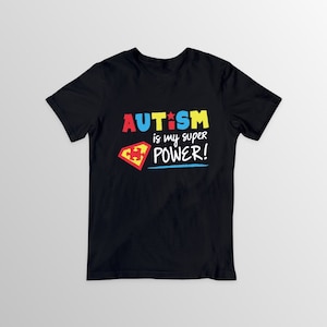 May include: Black t-shirt with the words "AUTISM is my SUPER POWER!" in colorful, bold letters. A red and yellow shield graphic with a puzzle piece is on the left side. The shirt is a crew neck style.