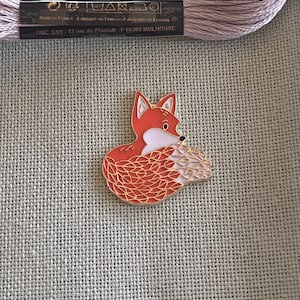 May include: A gold-colored enamel pin featuring a red fox curled up with its tail wrapped around its body. The fox has white accents on its face and tail.