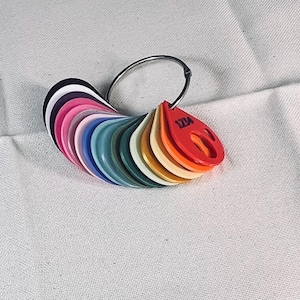 May include: A color swatch ring featuring a variety of colors, including black, pink, blue, and orange. The swatches are attached to a silver metal ring. The red swatch has the text "123A" printed on it. The swatches are arranged in a fan shape.